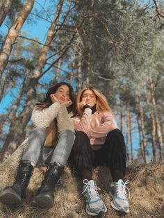 two young women sitting on top of a pile of hay in the middle of a forest