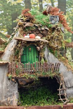 a house made out of wood and moss with a green door in the middle surrounded by trees