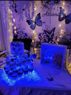 a table topped with cupcakes covered in frosting and lit up butterfly decorations