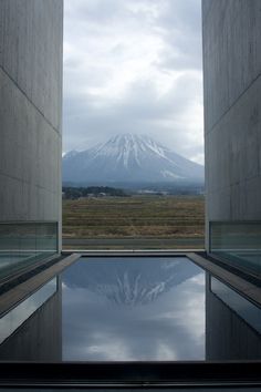 an empty pool in front of a mountain with snow on the top and clouds reflected in it