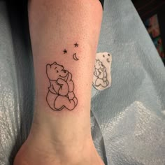 a small tattoo on the foot of a person with a teddy bear and moon behind it