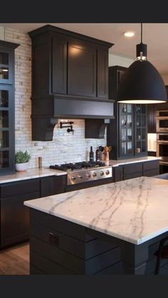 a large kitchen with black cabinets and marble counter tops, along with stainless steel appliances