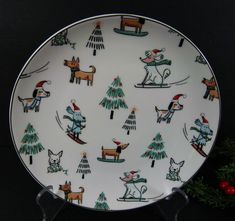 a white plate with dogs and trees on it, sitting next to a christmas tree