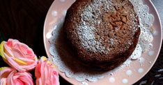 two chocolate cakes are on a plate with pink flowers next to it and one is covered in powdered sugar