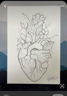 a drawing of a heart with flowers in it on a piece of paper next to some mountains