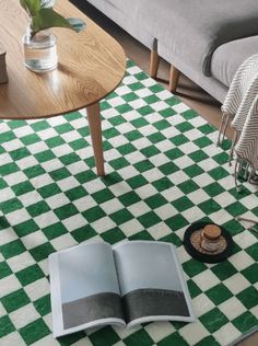 an open book sitting on top of a green and white checkered rug next to a coffee table