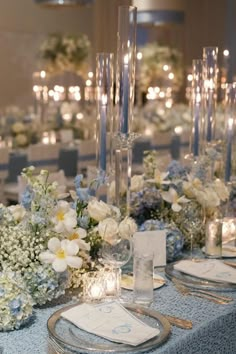 the table is set with white and blue flowers, candles, and napkins on it