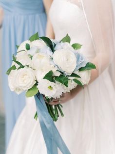 two bridesmaids holding bouquets of white and light blue flowers in their hands