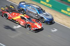 two cars racing on a race track with each other in the same direction, one driving behind another