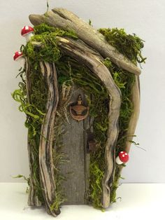 a fairy house made out of driftwood and moss with red mushrooms on the door