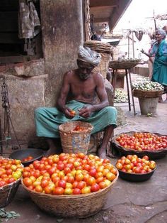 a man sitting on the ground next to baskets filled with tomatoes and other fruit items