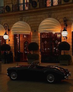 an old car parked in front of a building at night with lights on the windows