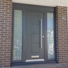 a man standing in front of a door with his reflection on the glass and brick wall behind him