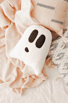 a white pillow with black eyes on top of a bed next to pillows and blankets