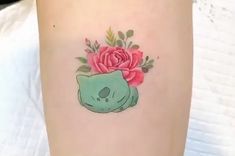 a tattoo with a skull and flowers on the side of her leg that has a rose in it