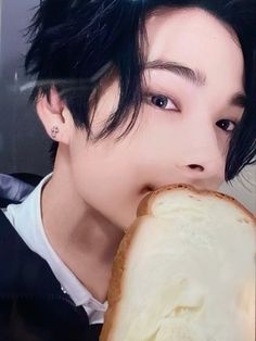 a man with black hair is eating a piece of bread in front of his face