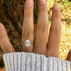 a woman's hand with a diamond ring on top of her finger next to a tree