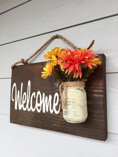 a mason jar with flowers is hanging on the wall next to a sign that says welcome