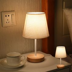 a table with a lamp, cup and saucer on it next to a light switch