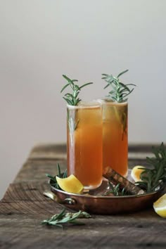 two glasses filled with lemonade and rosemary garnish on top of a wooden table