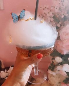 a woman holding up a cup filled with ice cream and butterflies on top of it