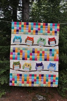 an owl themed quilt hanging on a clothes line with trees in the backgroud