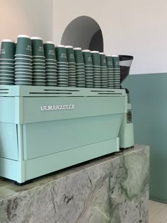 many cups are stacked on top of each other in front of a coffee maker and counter