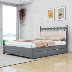 a bed sitting on top of a hard wood floor next to a white wall with pictures above it