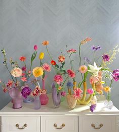 a white dresser topped with lots of vases filled with flowers