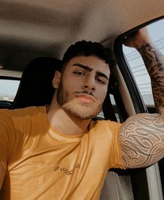 a man with tattoos on his arm sitting in the back seat of a car looking at the camera