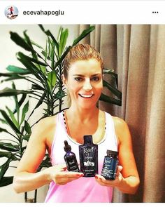 a woman holding three bottles of essential oils in front of a potted palm tree