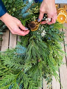 someone is making a pine cone wreath with oranges and greenery on the table