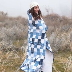 a woman is standing in the grass wearing a blue and white quilt