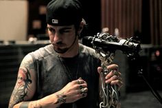 a man with tattoos on his arm holding a metal object in one hand and looking at the other