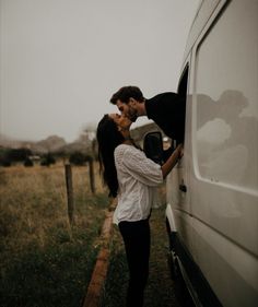 a man and woman kissing in front of a white van on the side of a road