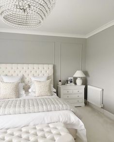 a white bed sitting under a chandelier next to a night stand and dresser