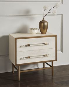 a white and gold chest of drawers next to a vase