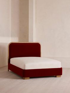 a red bed with gold studded headboard and foot board in an empty room