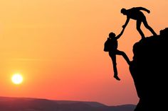 two people are climbing up the side of a cliff at sunset or sunrise, with one person holding onto another man's hand