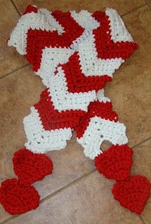 a crocheted red and white blanket laying on the floor next to two hearts