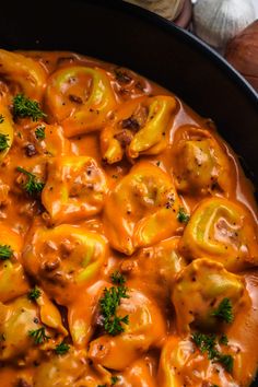 a skillet filled with pasta covered in cheese and sauce, garnished with parsley