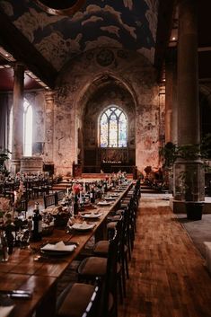 a long table with place settings in front of a stained glass window and wooden floor