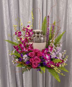 a vase filled with purple flowers and greenery on top of a table next to a curtain