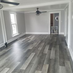 an empty room with hard wood flooring and fan in the corner, next to two windows