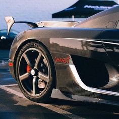 a black sports car parked on the street next to some water and umbrellas in the background