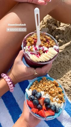 two people sitting on the beach eating ice cream and fruit sundaes with strawberries