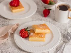 two white plates topped with slices of cake and strawberries next to a cup of coffee