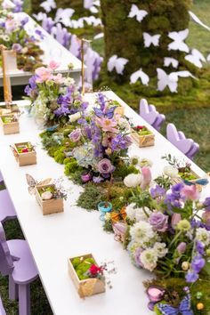 a long table with purple and white flowers on it is set up for an outdoor event