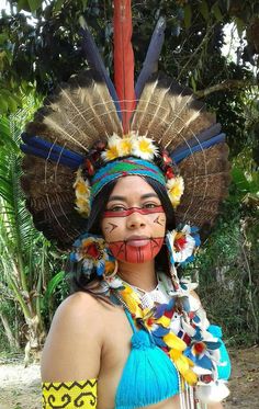 a woman with painted face and headdress standing in front of some trees,