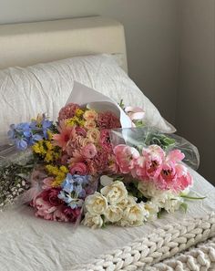 a bouquet of flowers is laying on the edge of a bed with a white blanket